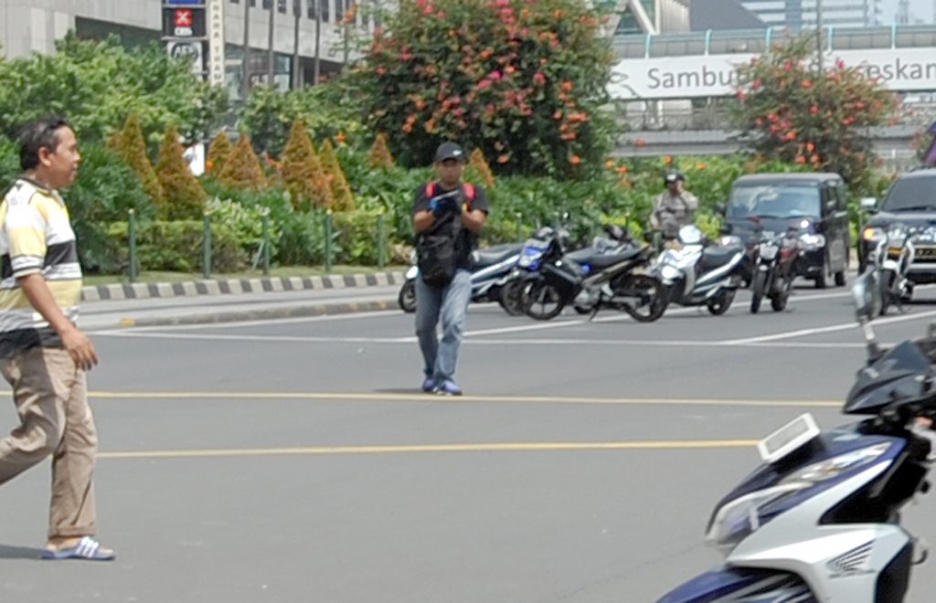 epa05101454 A man (C), who is believed to be a terrorist, holds a gun after a bomb blast in front of a shopping mall in Jakarta, Indonesia, 14 January 2016. Explosions near a shopping centre in the Indonesian capital Jakarta killed at least six people on 14 January, television reports and witnesses said. Police exchanged fire with suspected attackers after the blasts at a traffic police post in front of the Sarinah shopping centre and a nearby Starbucks coffee shop, media reported. EPA/ALFIAN BEST QUALITY AVAILABLE